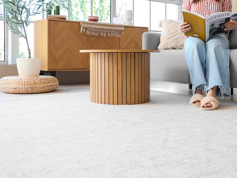 Woman in slippers reading magazine on sofa and soft carpet at home